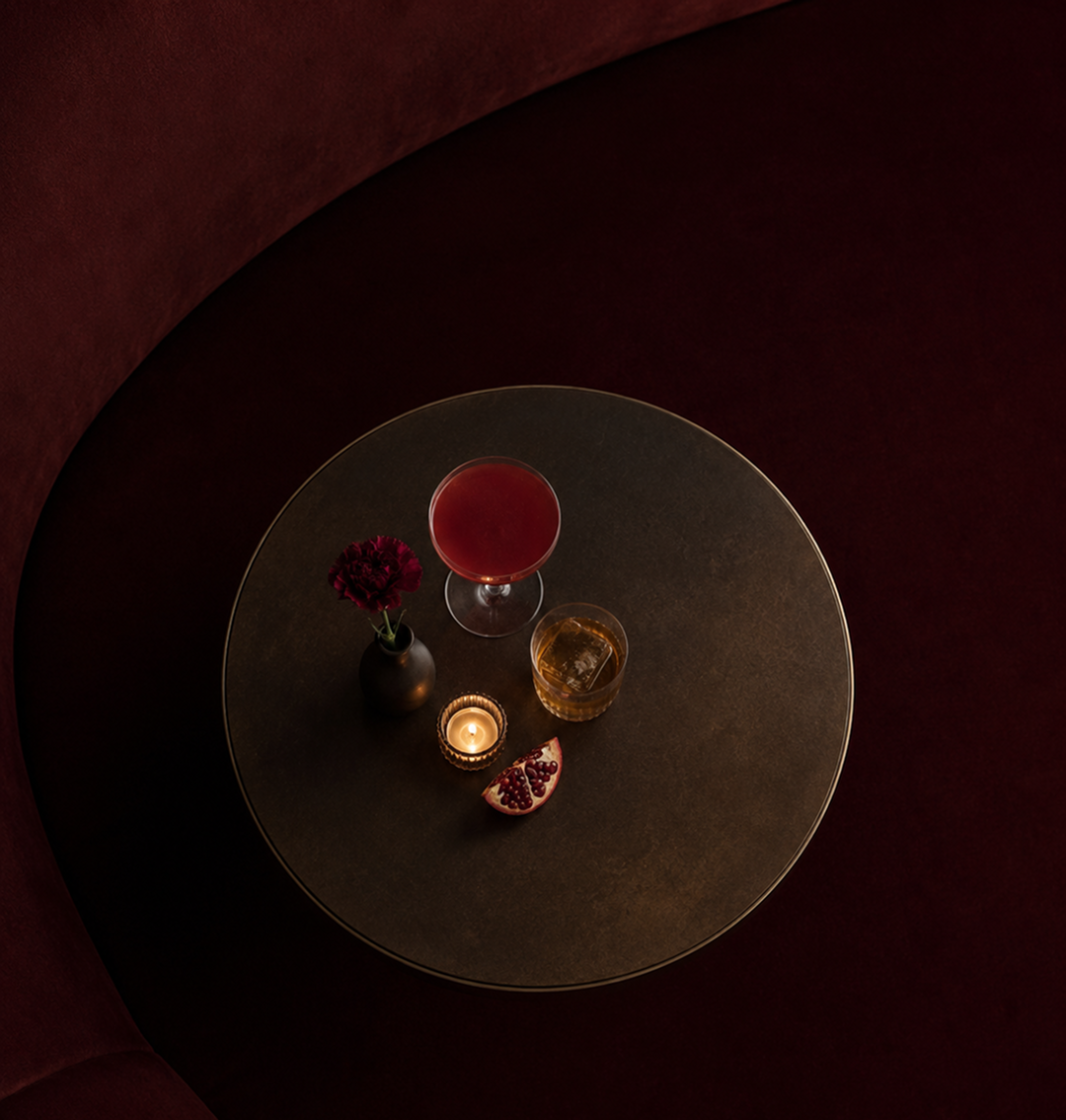 Overhead view of a round brass table with cocktails and a candle against deep red velvet
