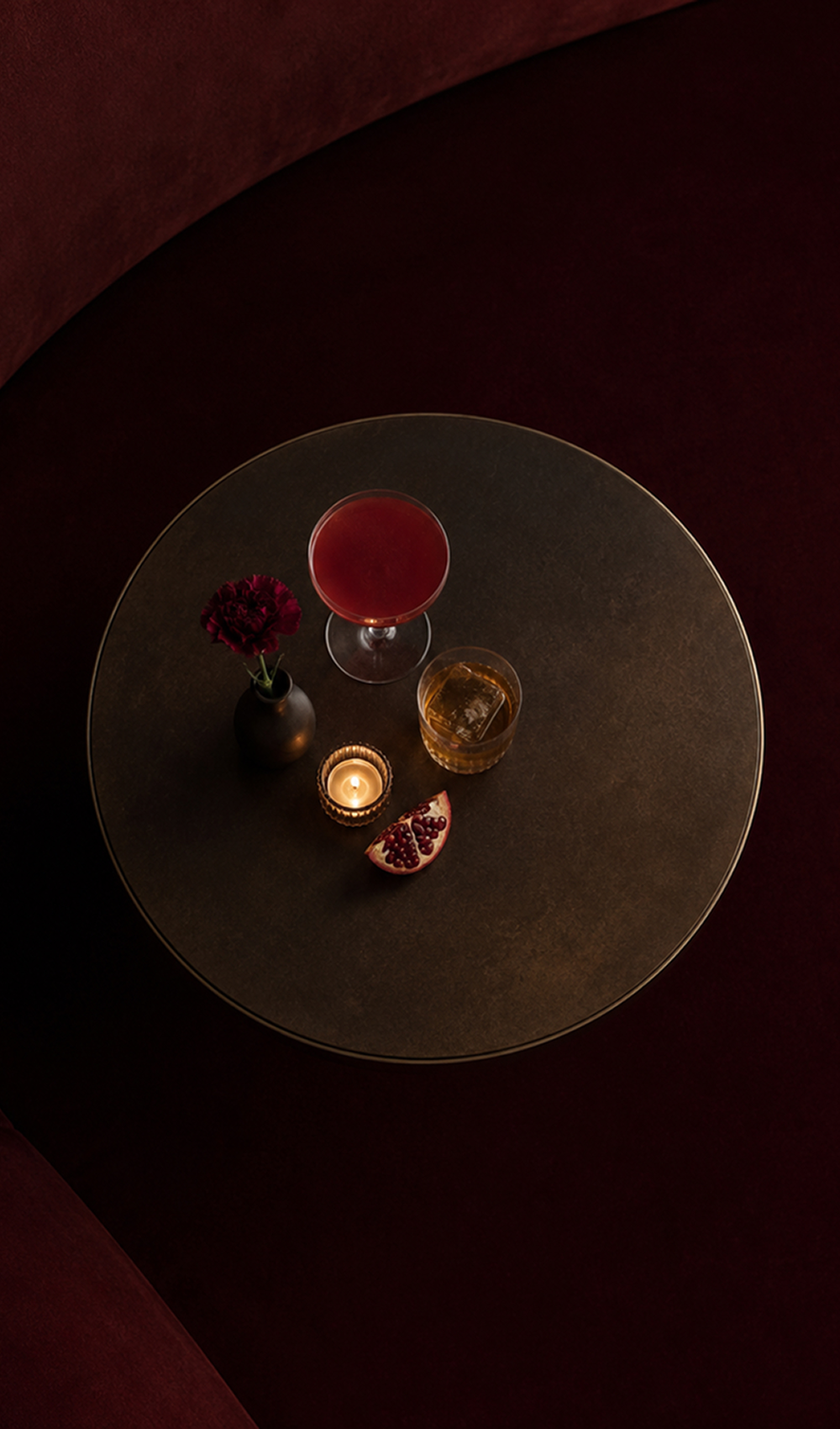 Overhead view of cocktails, a candle and pomegranate on a bronze table