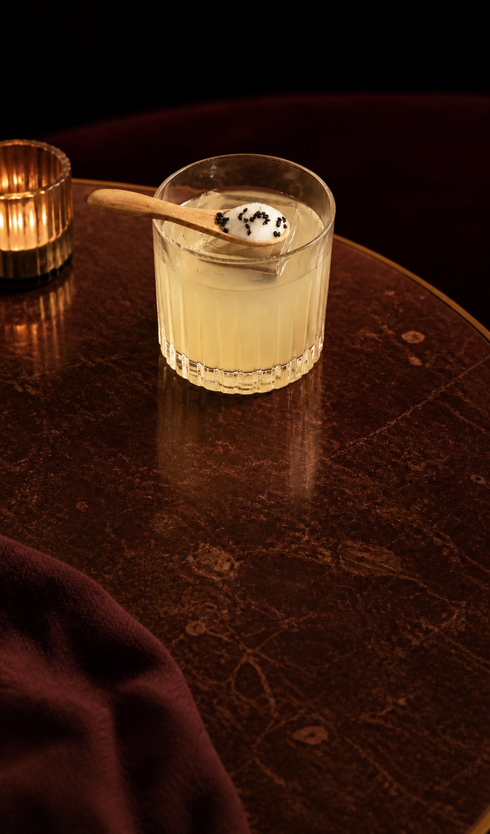 Pale citrus cocktail on the rocks with a sesame-topped spoon